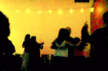 Fotografía intervenida en tono amarillo cálido: siluetas de dos parejas bailando tango bajo un cordón de luces, figuras oscuras en primer plano.